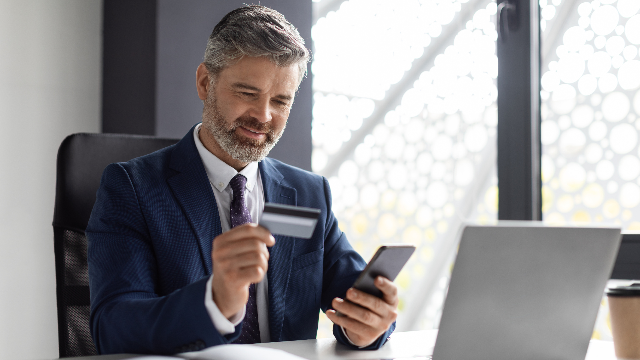 Middle Aged Businessman Using Smartphone And Credit Card In Office