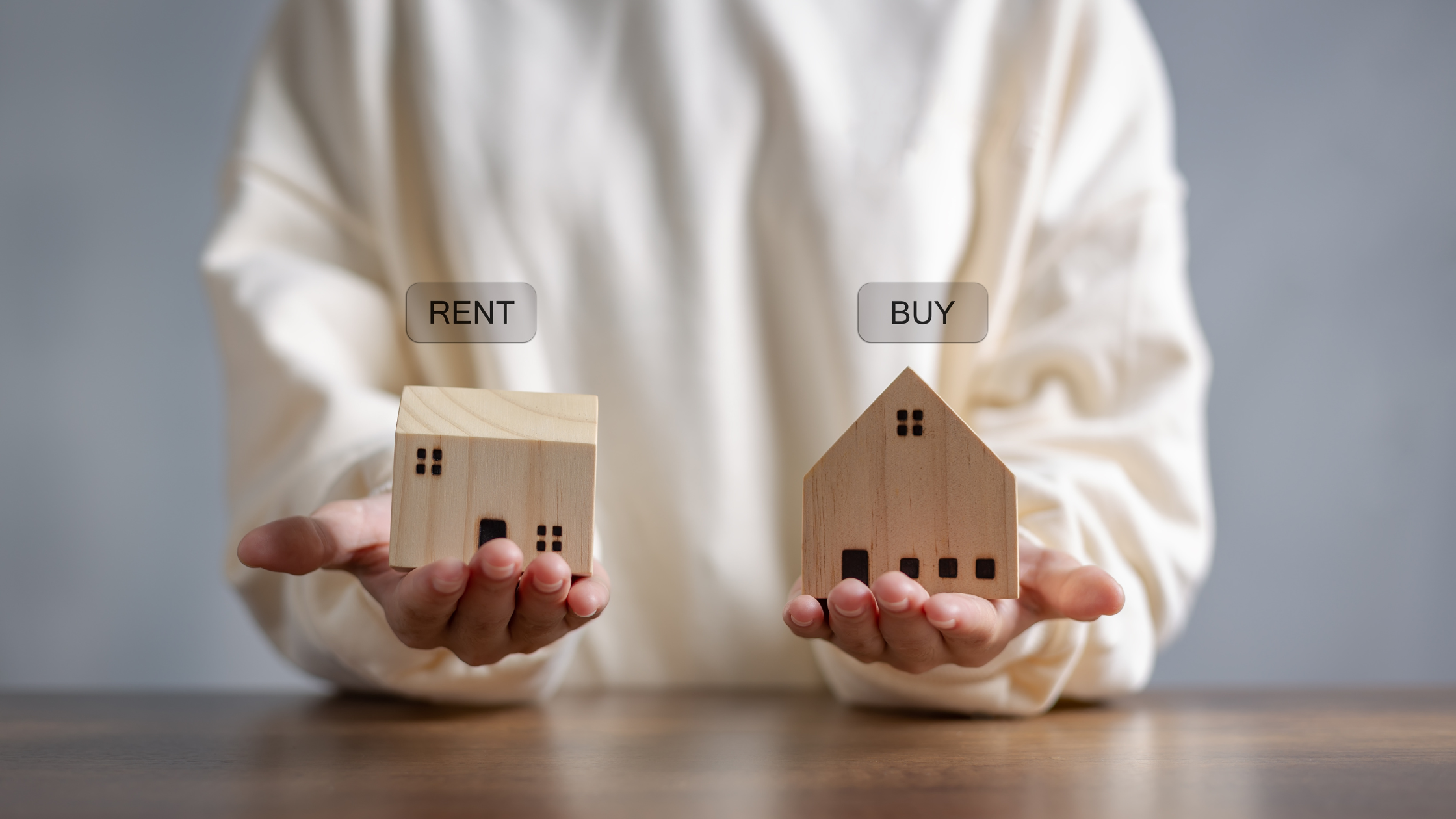 Person holding two houses, one to rent and one to buy